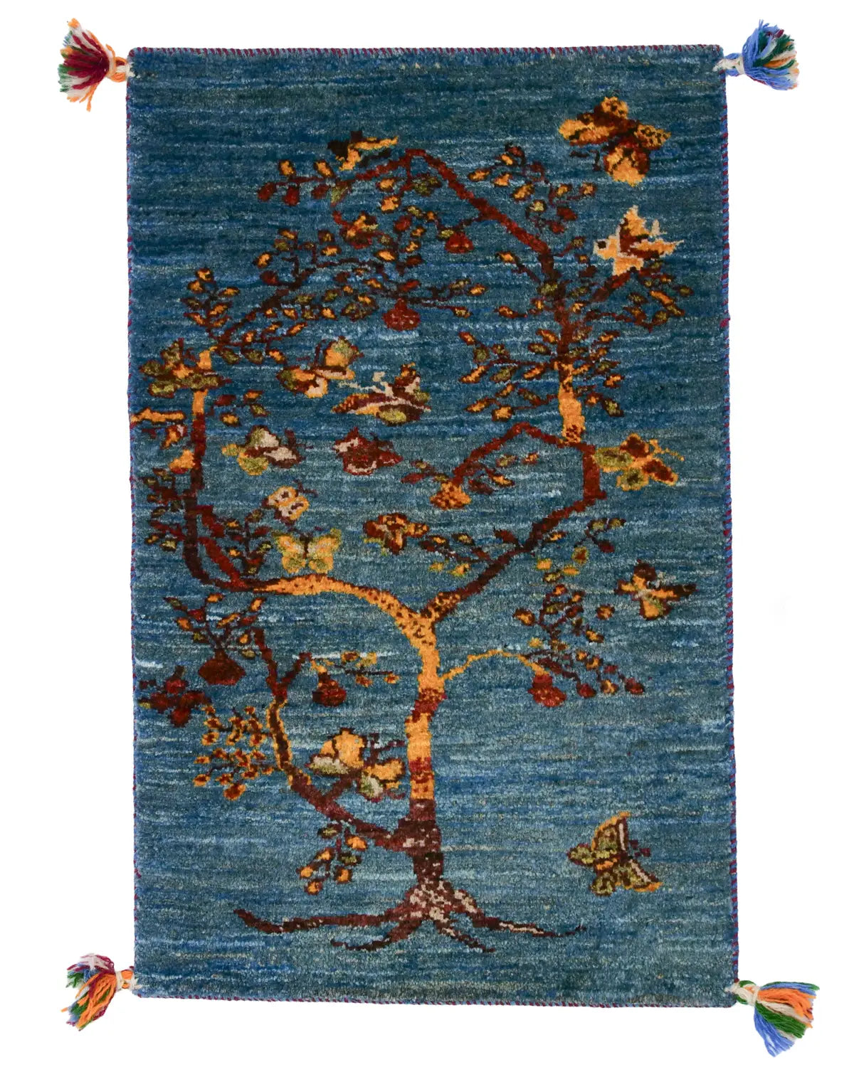 青い背景に生命力あふれる一本の木が描かれたギャッベ