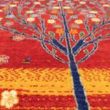 赤い背景に、青い幹と黄色や青の花が映える生命の樹デザインのギャッベ