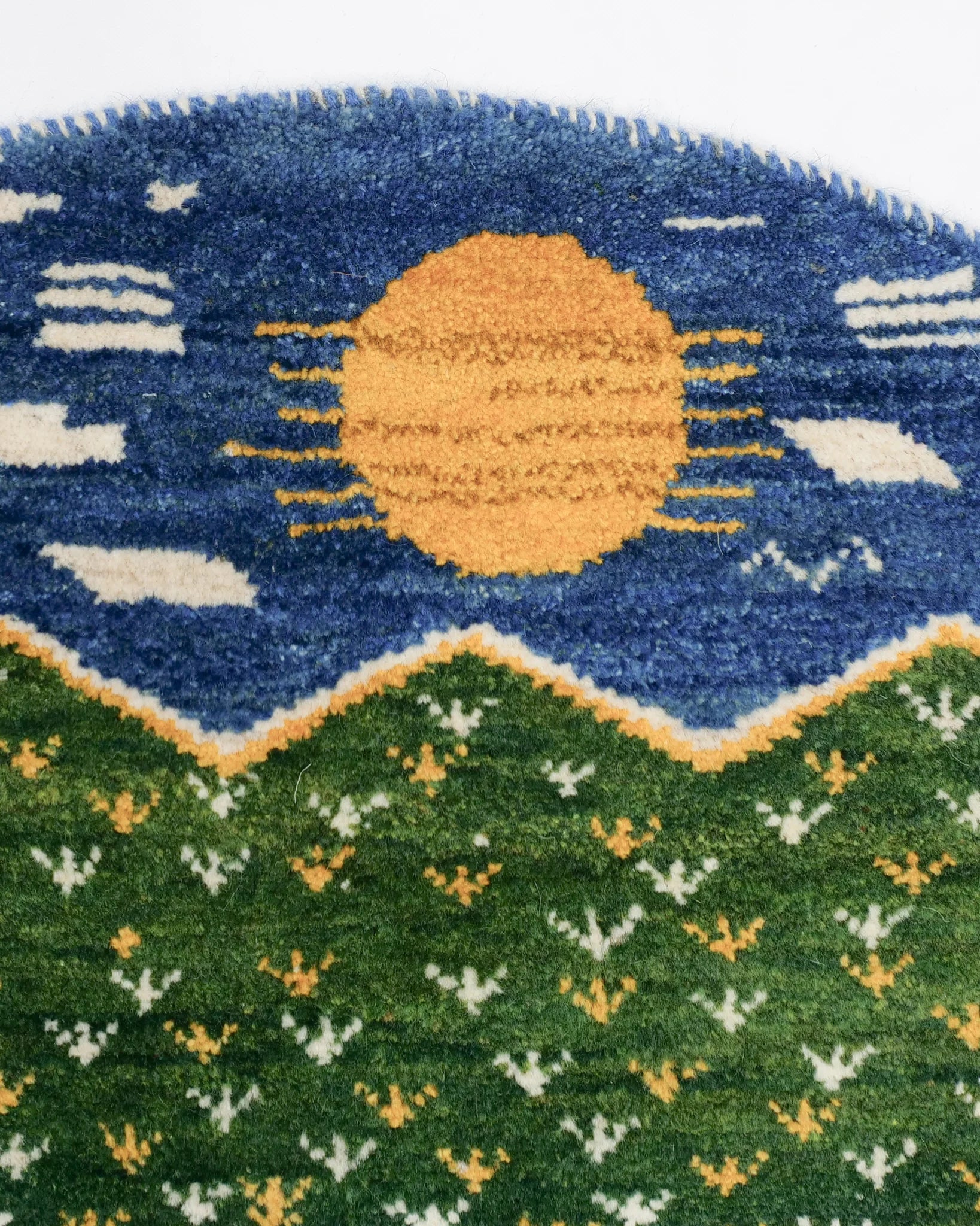 青地に黄色い太陽と白い雲を描いた円形ライオンギャッベの上端部分。