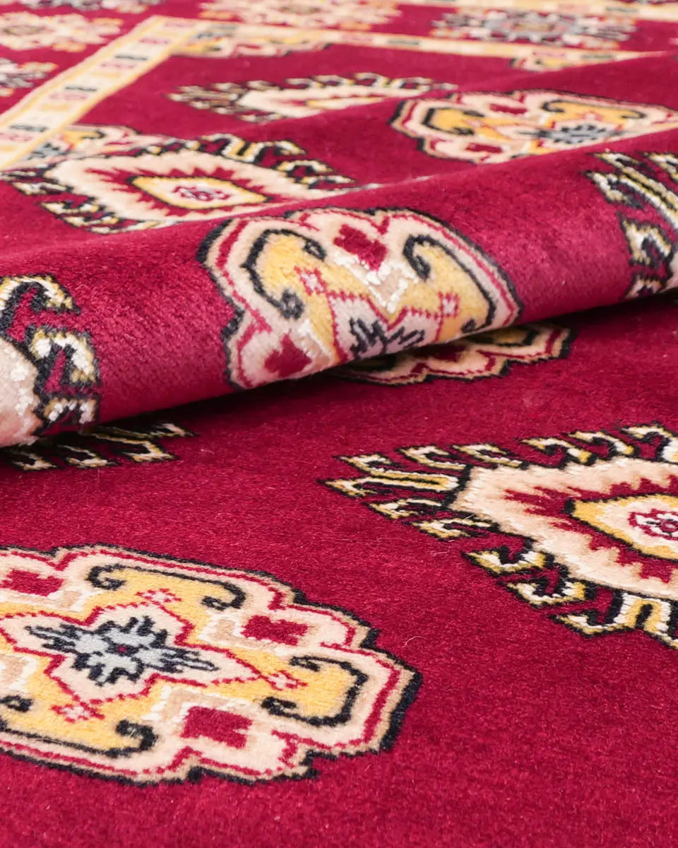 赤を基調としたパキスタン絨毯。中央にはひし形のジャルダン柄と楕円形のボハラ柄が交互に並び、周囲は繊細な模様で縁取られている。