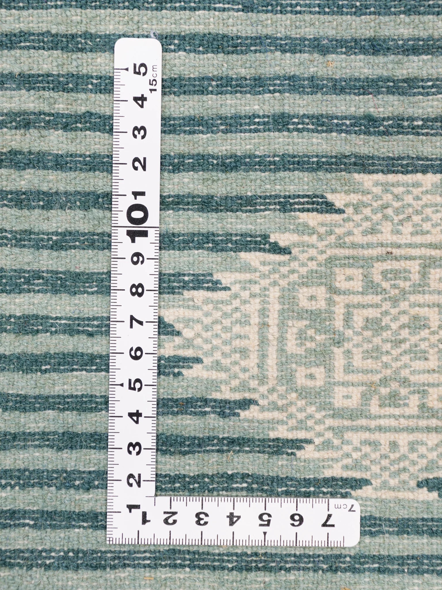 パキスタン絨毯の模様を定規で計測している写真。ストライプと幾何学柄の細部。