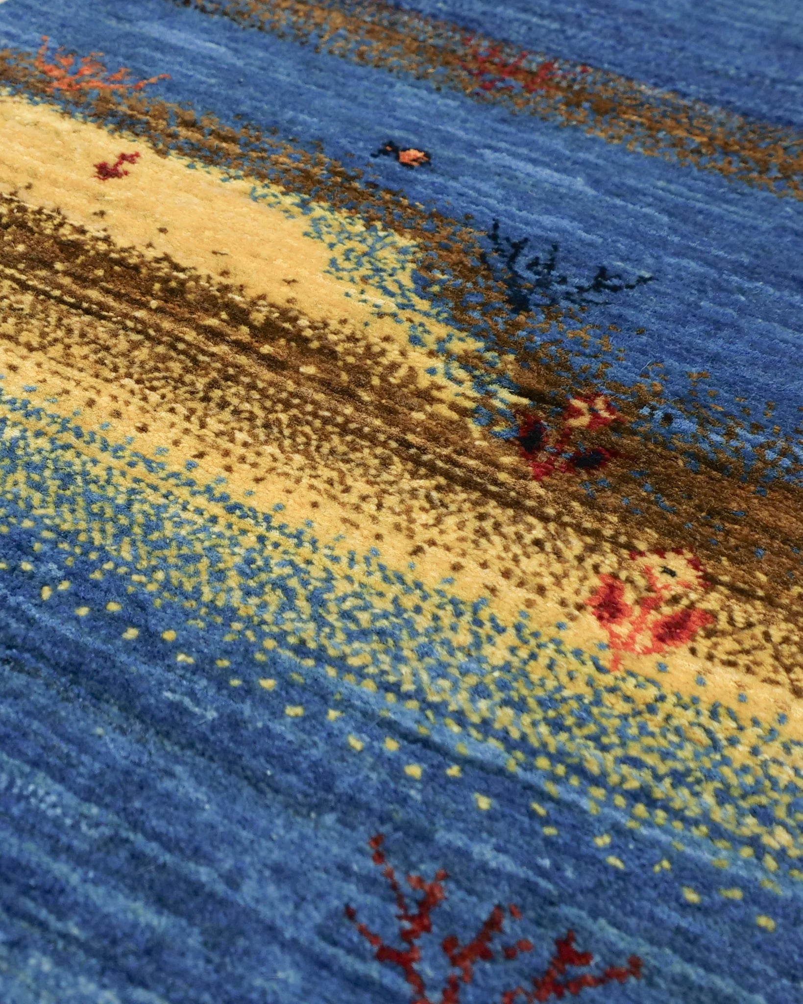シーラーズ産の手織りギャッベ。51×150cmのランナーサイズで、藍色の地に花や木々が咲き、中央には小さな魚とサンゴが織り込まれた水中風景が描かれている。