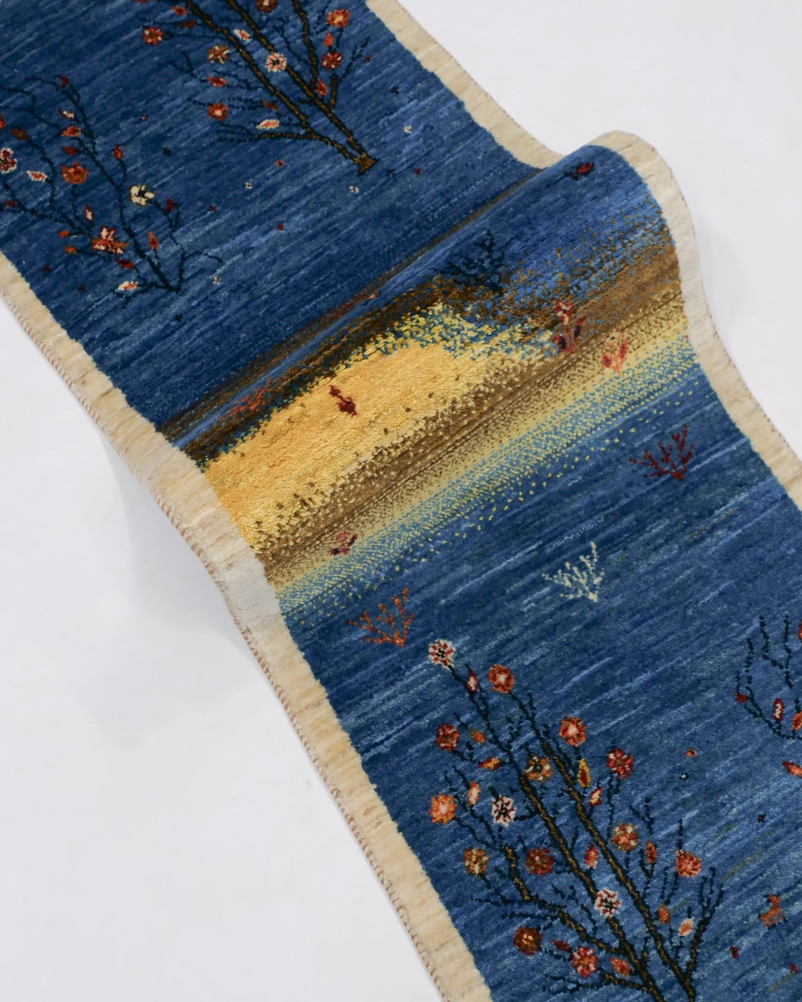 シーラーズ産の手織りギャッベ。51×150cmのランナーサイズで、藍色の地に花や木々が咲き、中央には小さな魚とサンゴが織り込まれた水中風景が描かれている。