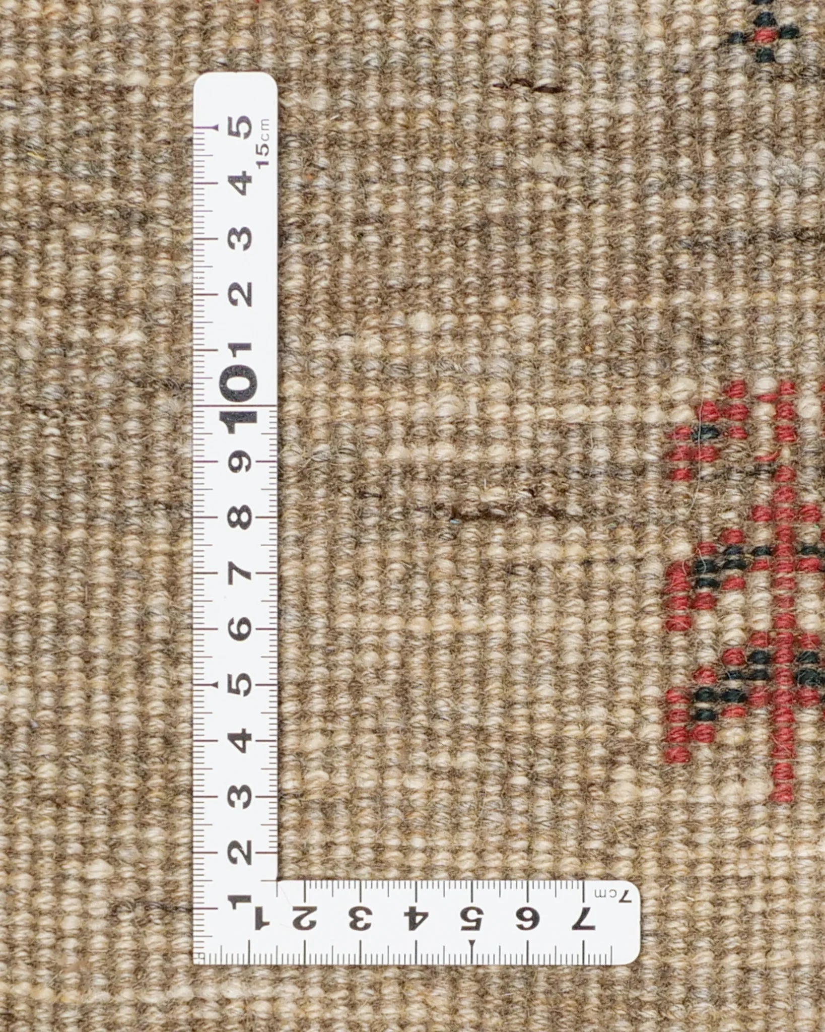 ギャッベの裏面を定規とともに撮影した画像。1平方センチあたりの織り密度が視覚的に分かる構成。赤い文様が一部見えている。