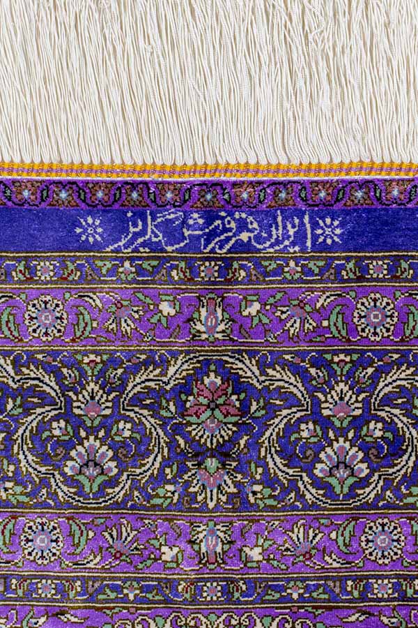 「イラン・クム製、手織りのファインクオリティペルシャ絨毯。商品番号 43745。シルク素材、約101cm x 103cmのサイズ（フリンジを含まず）。正方形に近く、パープルの色合わせのデザイン。中央のレンゲ風メダリオンとその周囲の白い花や唐草模様が細かく緻密に織り込まれている。サイン