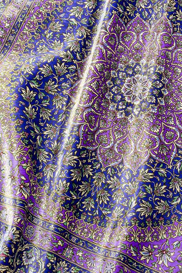 「イラン・クム製、手織りのファインクオリティペルシャ絨毯。商品番号 43745。シルク素材、約101cm x 103cmのサイズ（フリンジを含まず）。正方形に近く、パープルの色合わせのデザイン。中央のレンゲ風メダリオンとその周囲の白い花や唐草模様が細かく緻密に織り込まれている。絨毯の光沢